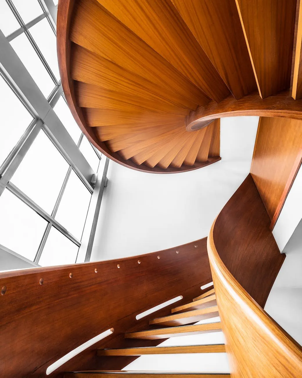 Walnut spiral stair seen from above next to a large window